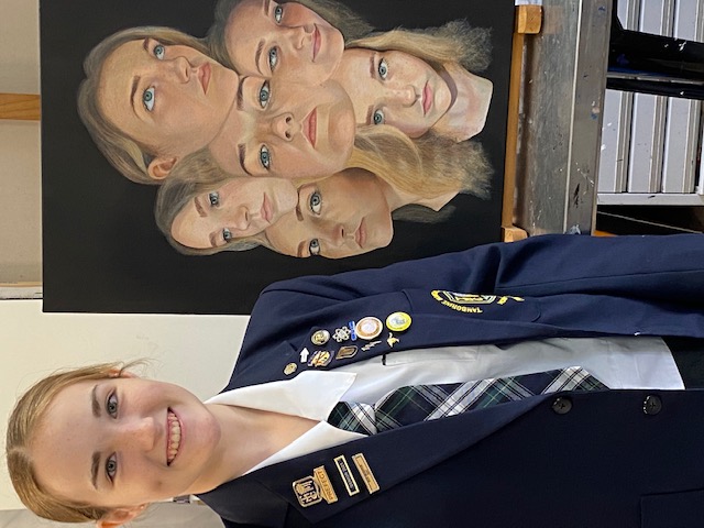 Hannah dalton year 12 student at tamborine mountain college with her painting behind the mask preparing for artsfest